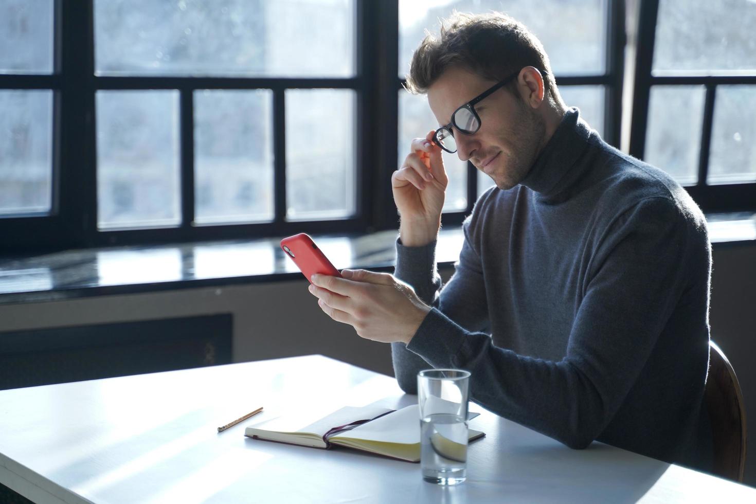 Attractive European male entrepreneur sitting at office table with mobile phone in hand photo