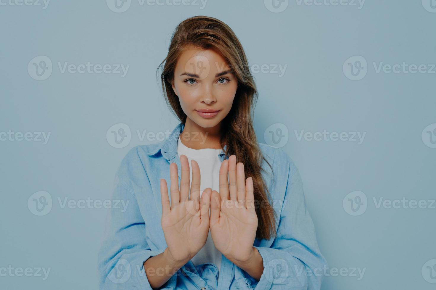 mujer seria que muestra gesto de parada sobre fondo azul claro foto