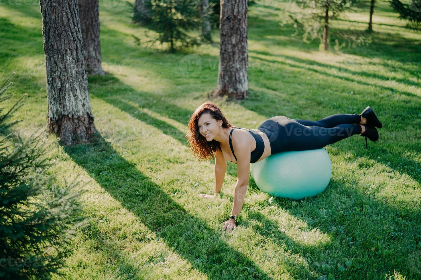 joven mujer deportiva complacida hace ejercicios de fitness con pelota de fitness, practica yoga en un parque verde o bosque, es instructora de aeróbic, se mantiene saludable y en forma. actividad física y gimnasia. foto