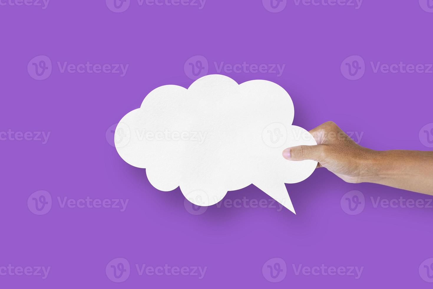 hand holding white paper cloud shape speech bubble balloon isolated on purple background communication bubbles photo