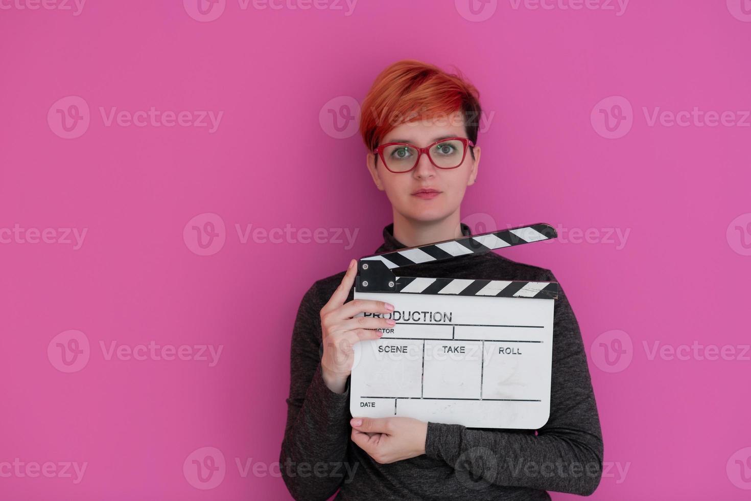 redhead woman holding movie  clapper on pink background photo