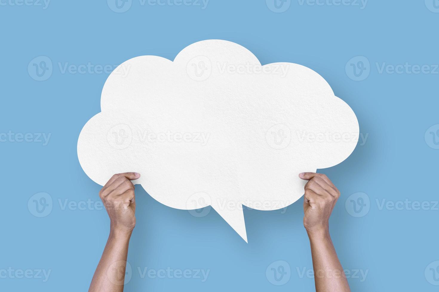 hand holding white paper cloud shape speech bubble balloon isolated on light blue background. photo