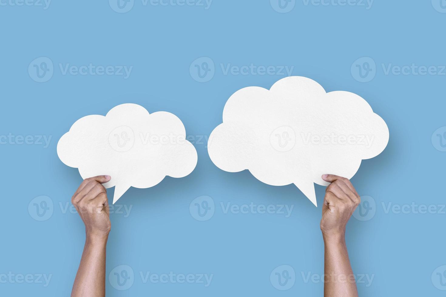 hand holding white paper cloud shape speech bubble balloon isolated on light blue background. photo