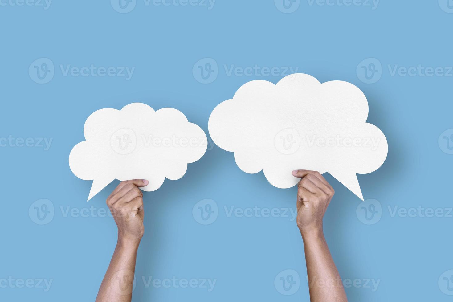 hand holding white paper cloud shape speech bubble balloon isolated on light blue background. photo