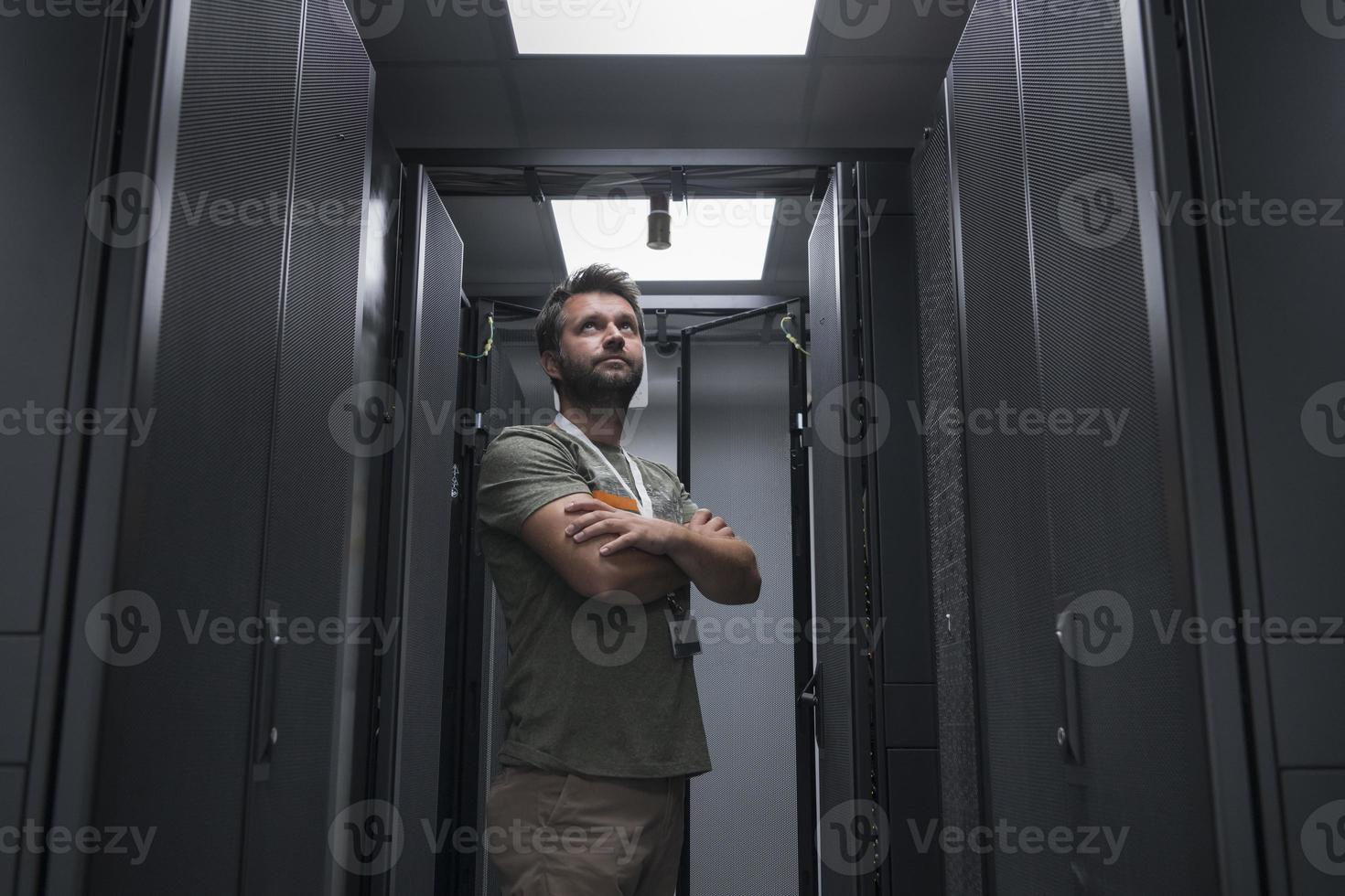 Portrait of male technician or network administrator standing brave as a hero with arms crossed in data center server room. photo