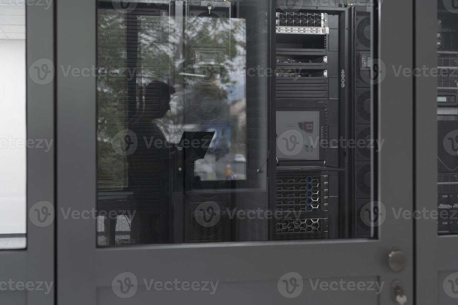 Software Engineer Working on a Laptop Computer in a Modern Server room. Monitoring Room Big Data Scientist in reflection of the entrance door. photo