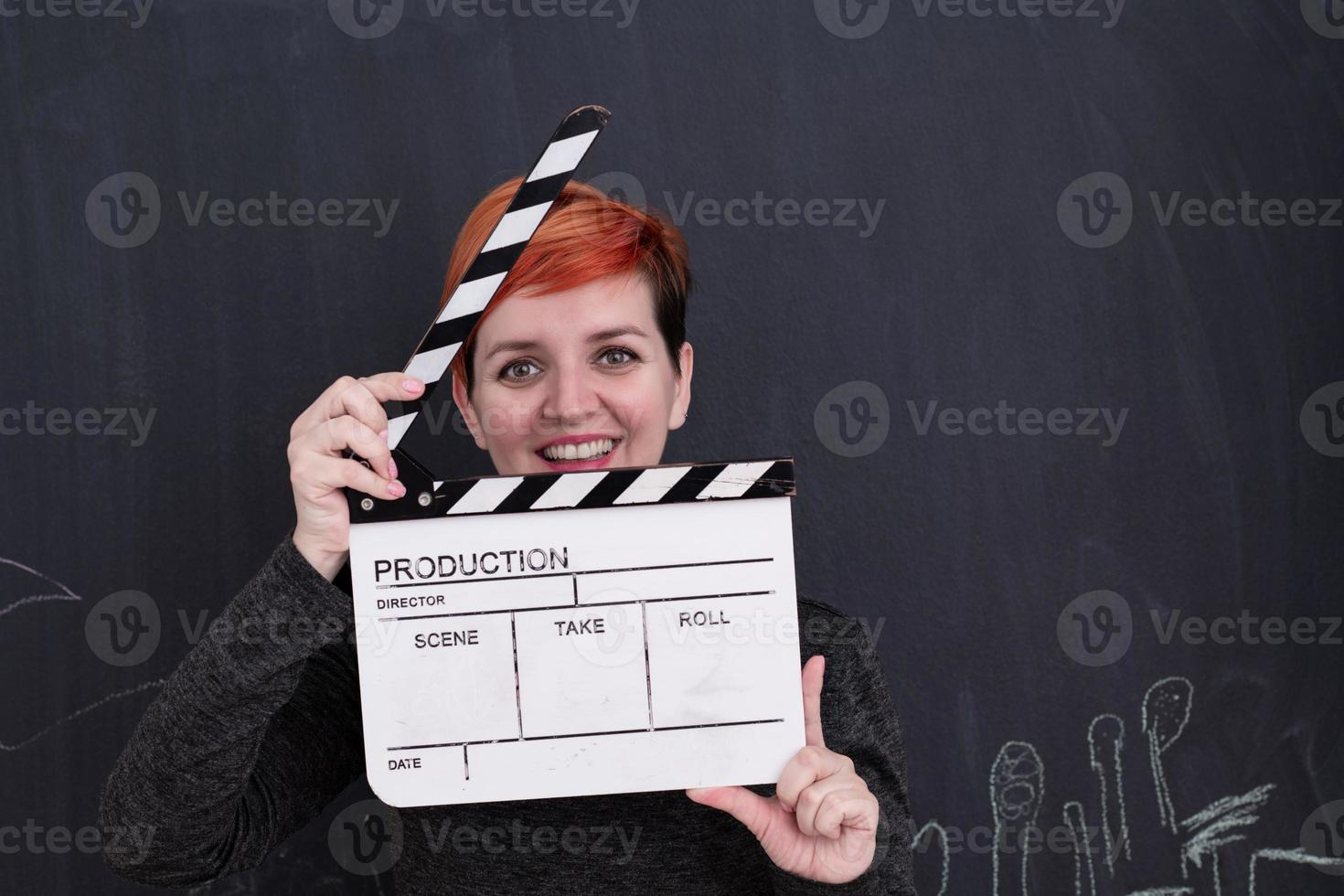 redhead woman holding clapper on black background photo