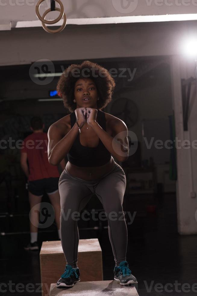 black female athlete is performing box jumps at gym photo