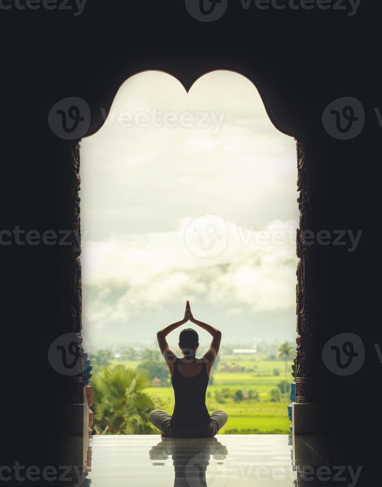 mujer de yoga sentada en posición de loto en el templo durante el amanecer, con reflejo en el suelo - efecto de color de estilo vintage foto