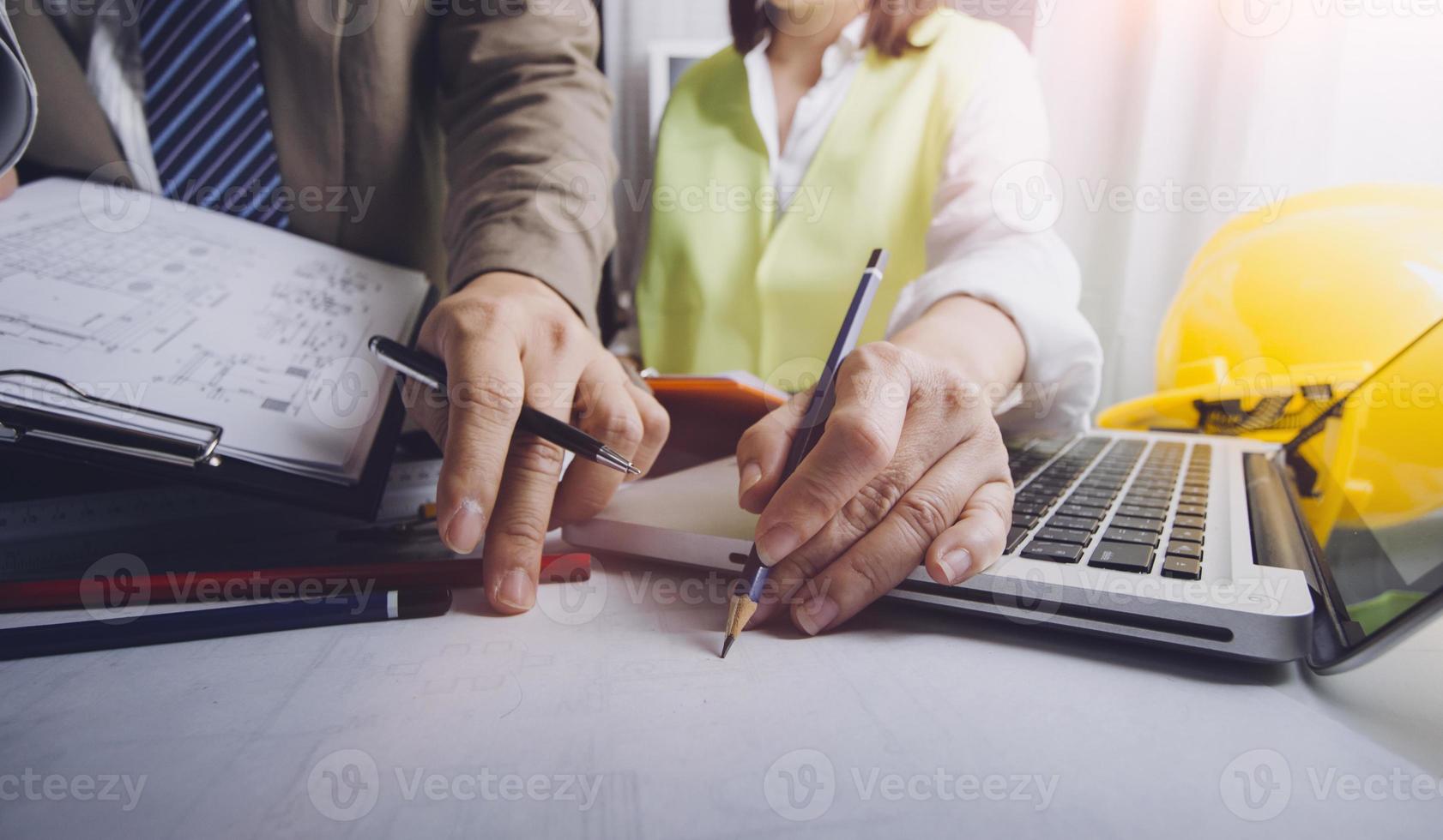 Two colleagues discussing data working and tablet, laptop with on on architectural project at construction site at desk in office photo