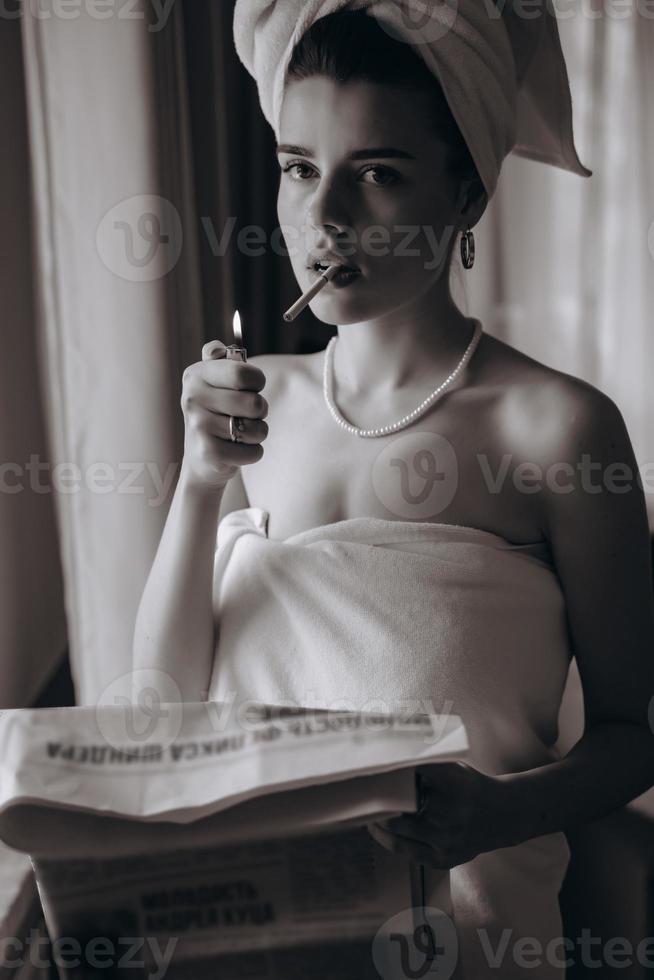 hermosa joven en una toalla fuma un cigarrillo y lee el periódico foto