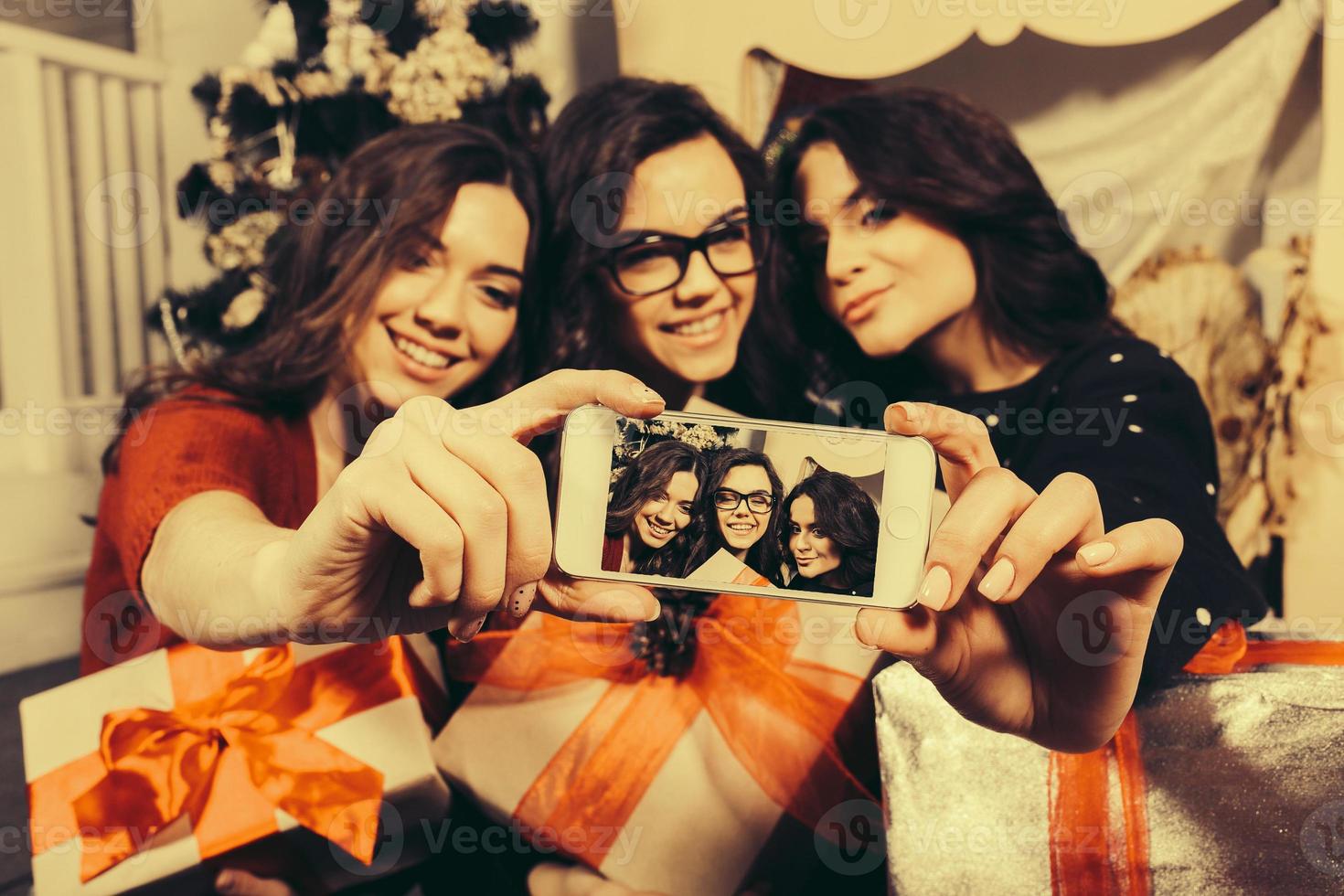 Beautiful girl photographed themselves on the phone on the background of Christmas gifts. Decorative vintage apartment. photo