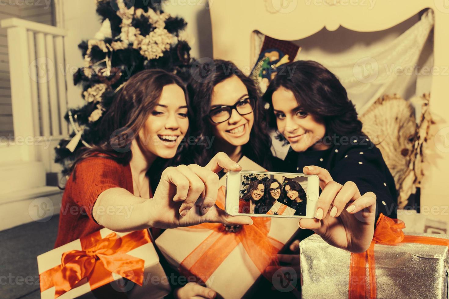 Beautiful girl photographed themselves on the phone on the background of Christmas gifts. Decorative vintage apartment. photo