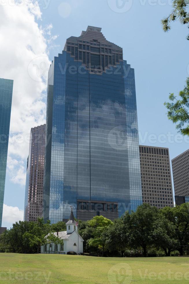 An old, white, wooden church juxtaposed against a modern glass skyscraper. photo