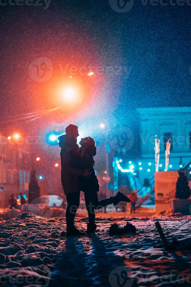 pareja de adultos jóvenes en los brazos del otro en la calle cubierta de nieve. foto