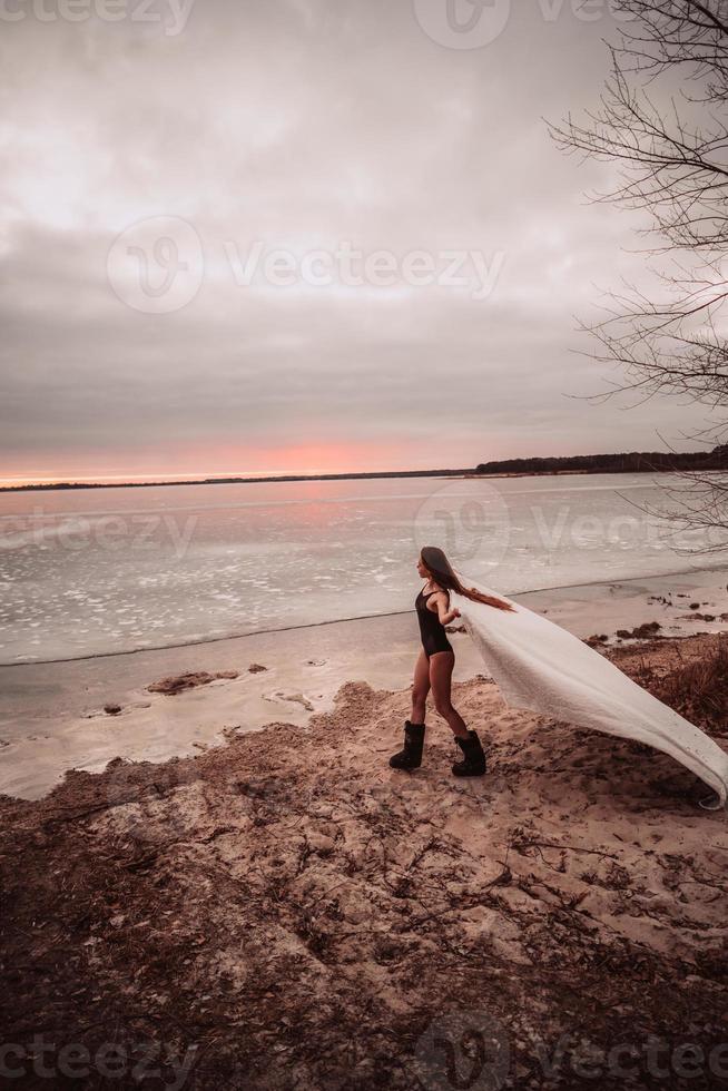 Beautiful young girl in a swimsuit on the shore of a frozen lake photo