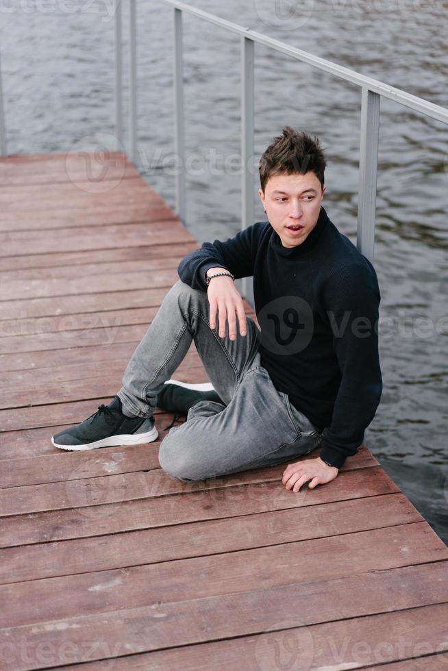 joven sentado en un muelle de madera foto