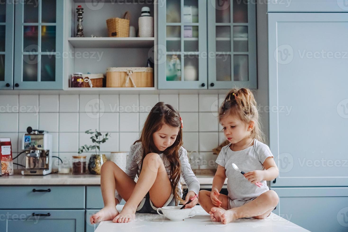 Two little girls in the kitchen sitting on the table. photo