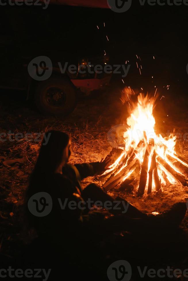 mujer sentada y calentándose cerca de la hoguera en el bosque nocturno. foto