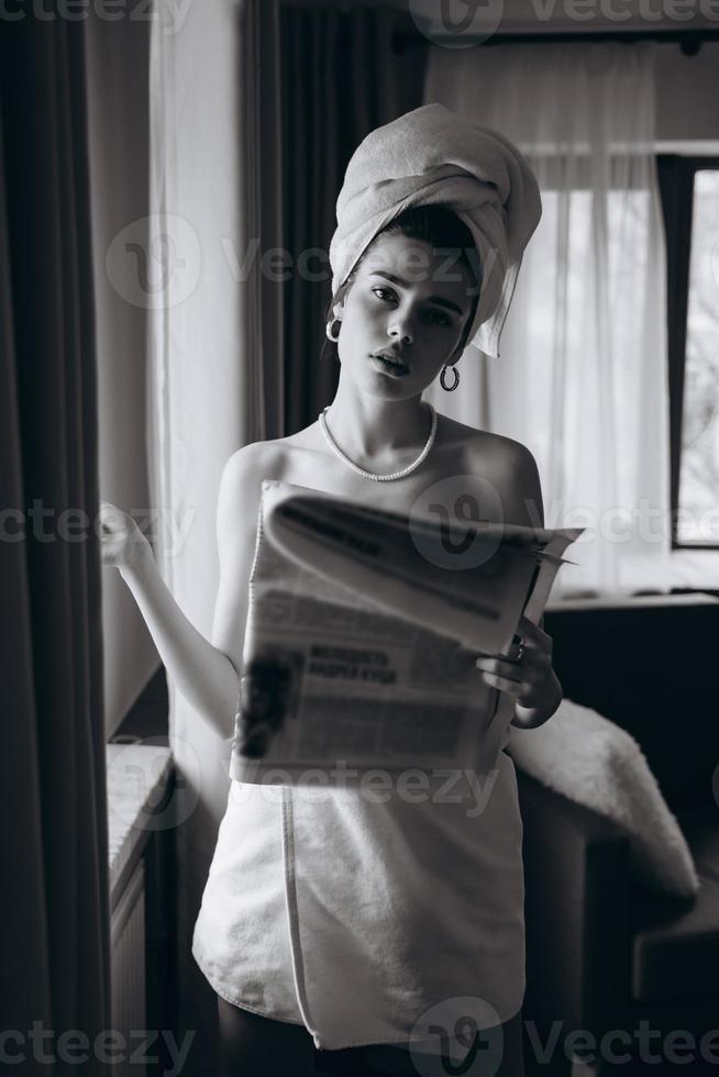 Beautiful young woman in a towel smokes a cigarette and reads newspaper photo