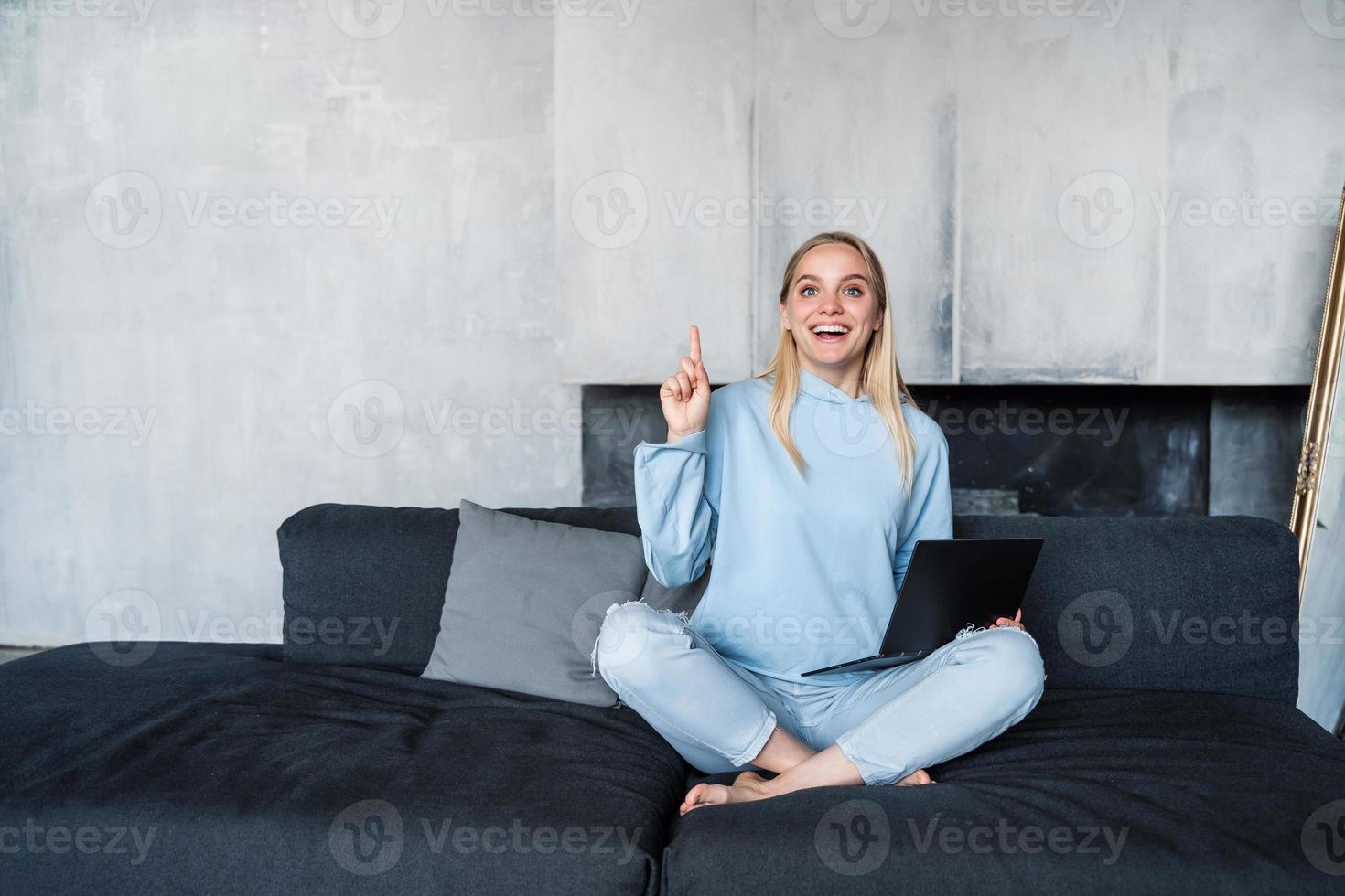 Image of happy woman using silver laptop while sitting on sofa photo