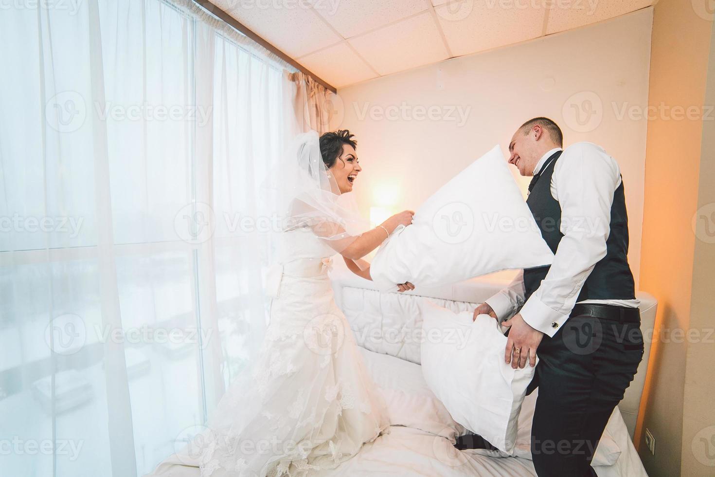 Pillow fight of bride and groom in a hotel room photo