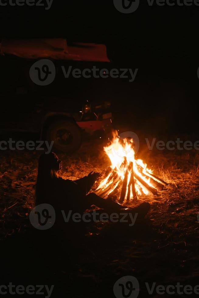 mujer sentada y calentándose cerca de la hoguera en el bosque nocturno. foto