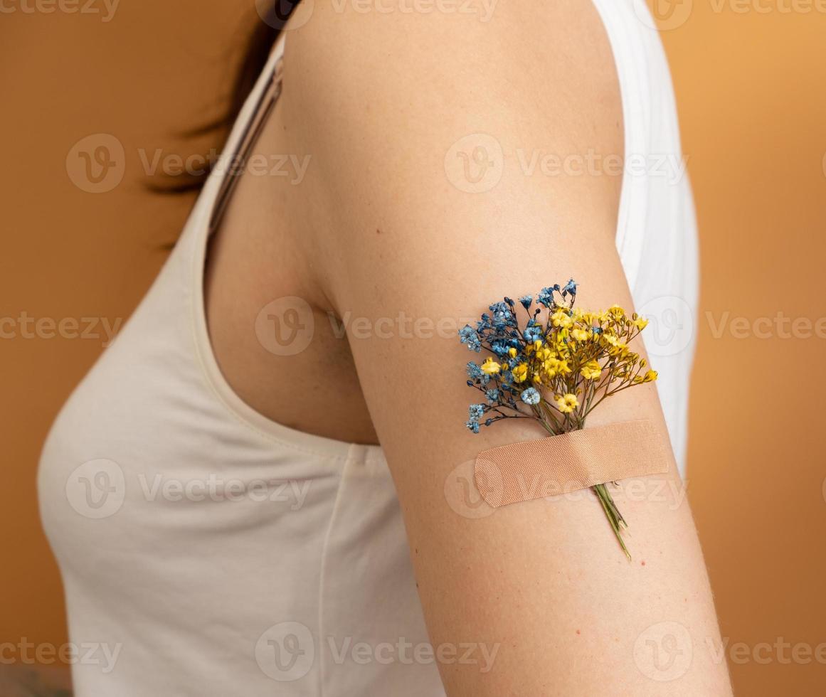 Blue and yellow flower under the patch on a woman's hand. The concept of vaccination and treatment in Ukraine photo