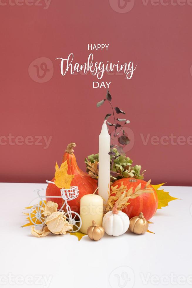 Autumn composition with Happy Thanksgiving Day greeting text. Dried leaves, pumpkins and candles on white pink background. photo