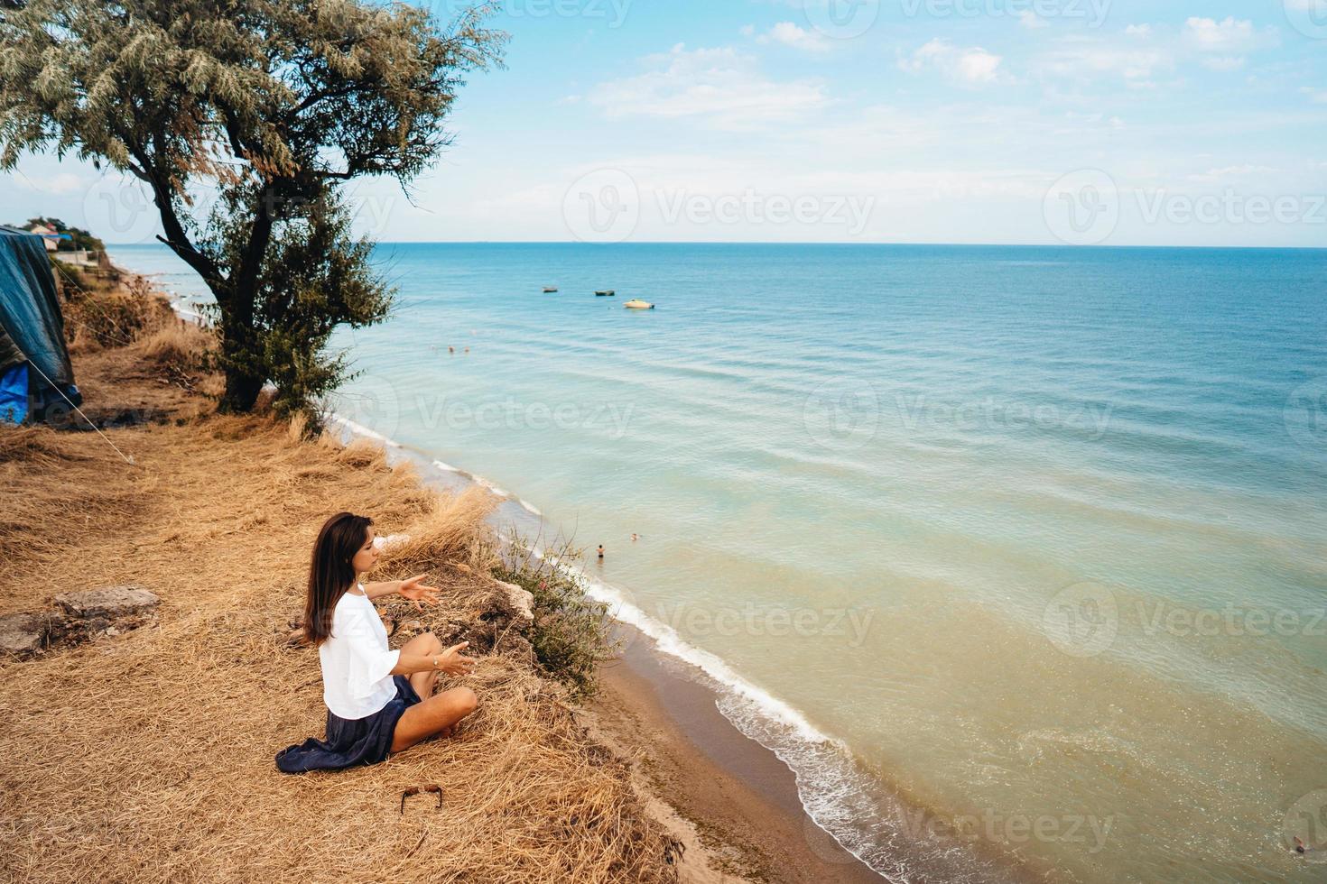 attractive woman in summer skirt and shirt sits on the shore photo