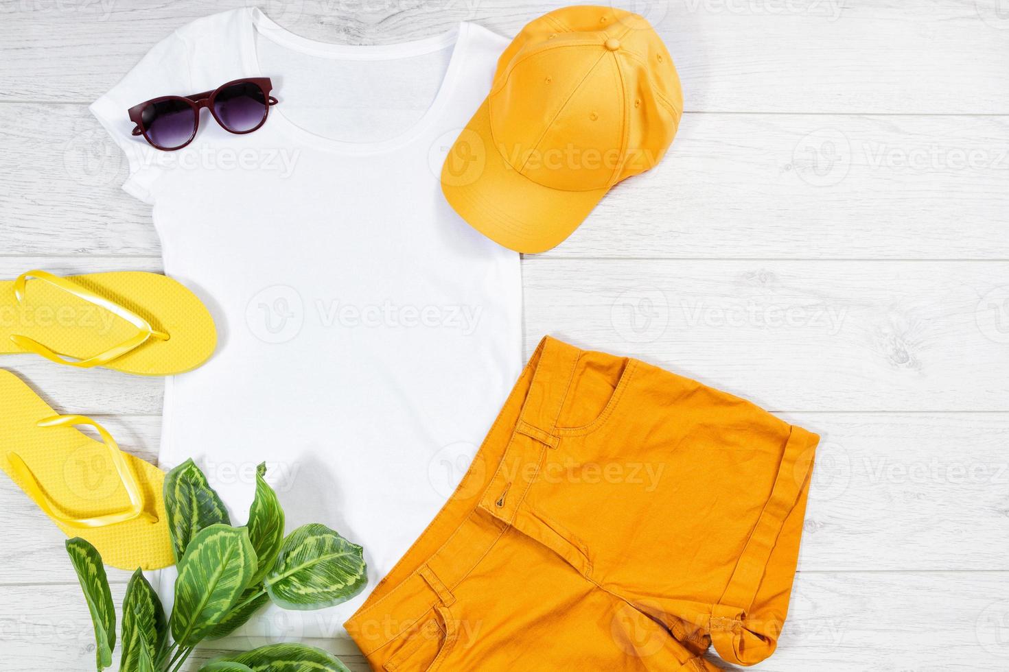 las chanclas blancas de la camiseta femenina se burlan planas sobre fondo de madera. vista superior y espacio de copia. camiseta de maqueta y verano. camisa en blanco de plantilla. sombrero amarillo foto