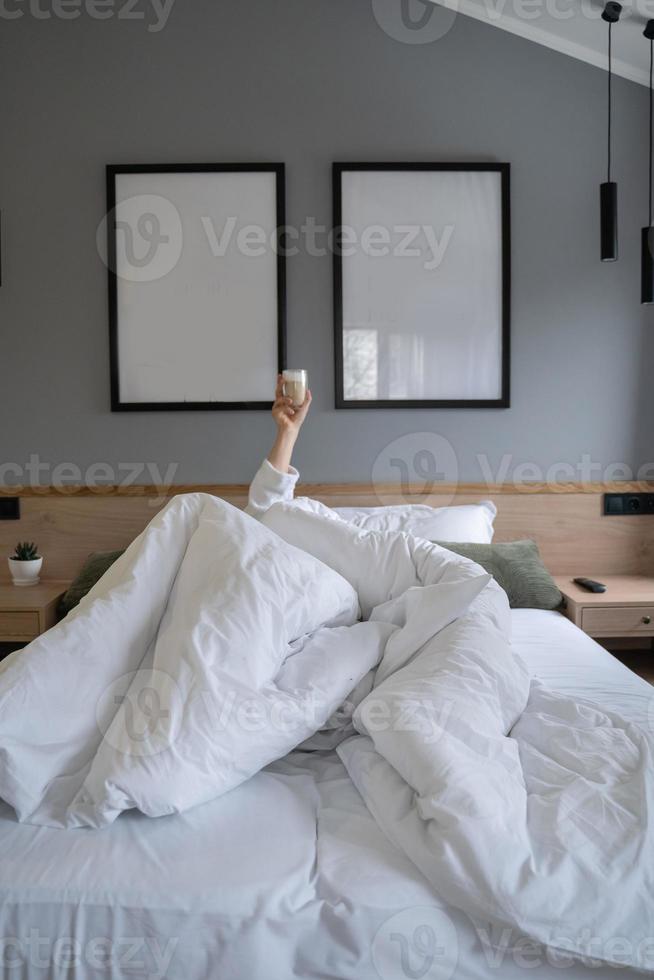 Hand holding a cup of coffee at home in bed photo