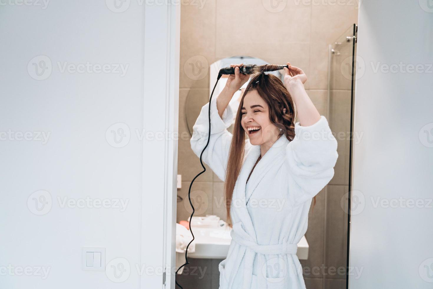 bella mujer sonriente rizando el cabello largo con rizador. foto