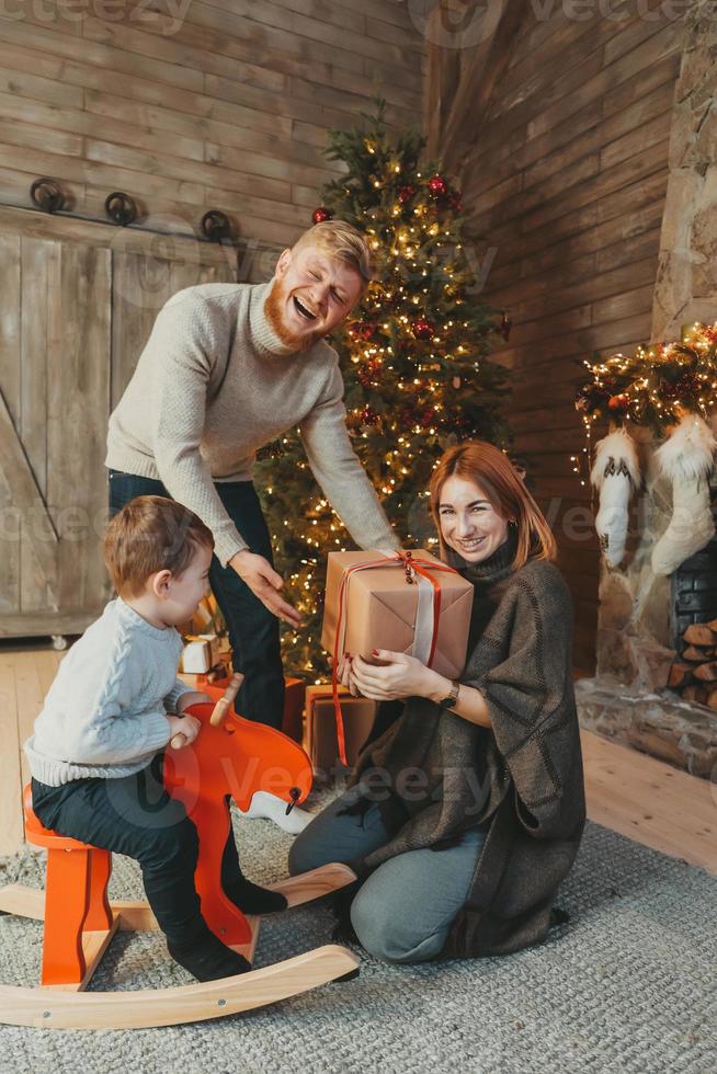 joven familia caucásica mamá papá hijo cerca de la chimenea árbol de navidad foto