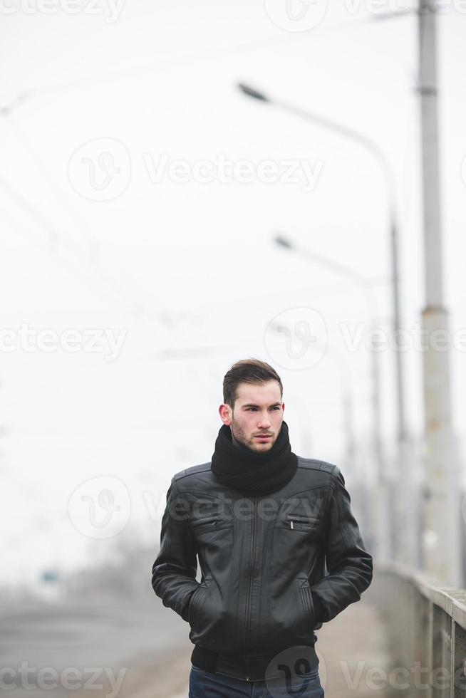 A man dressed in jeans and jacket stands near the main road in foggy weather photo