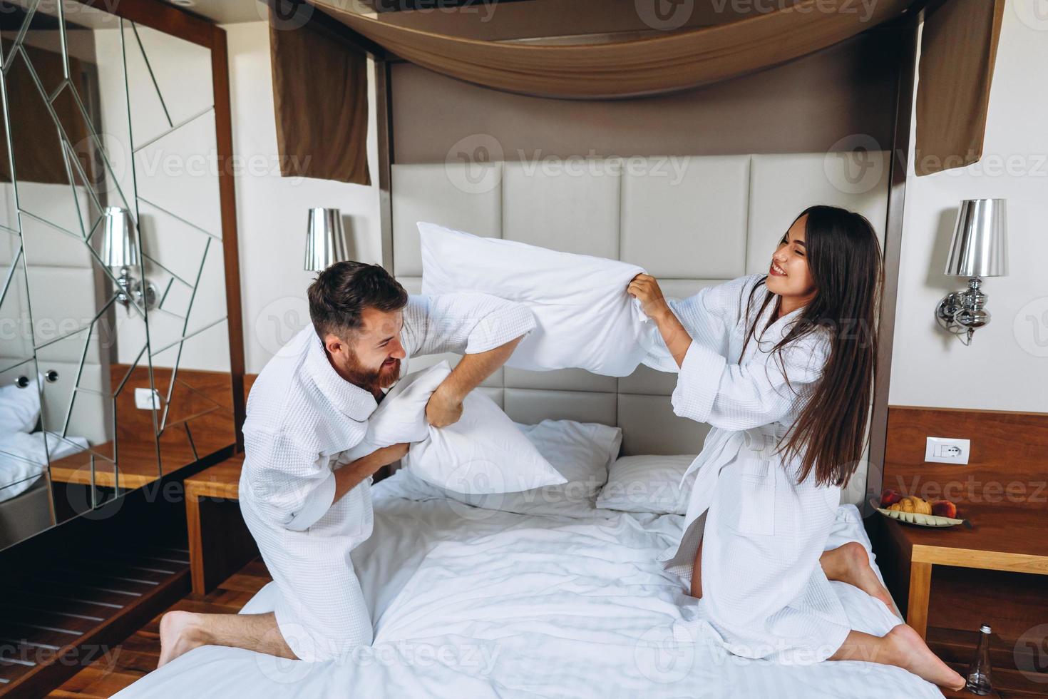 Cheerful couple have fun in the bedroom fighting with big pillows at home photo