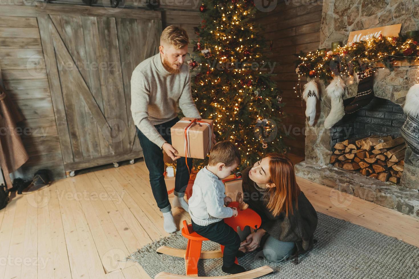 joven familia caucásica mamá papá hijo cerca de la chimenea árbol de navidad foto