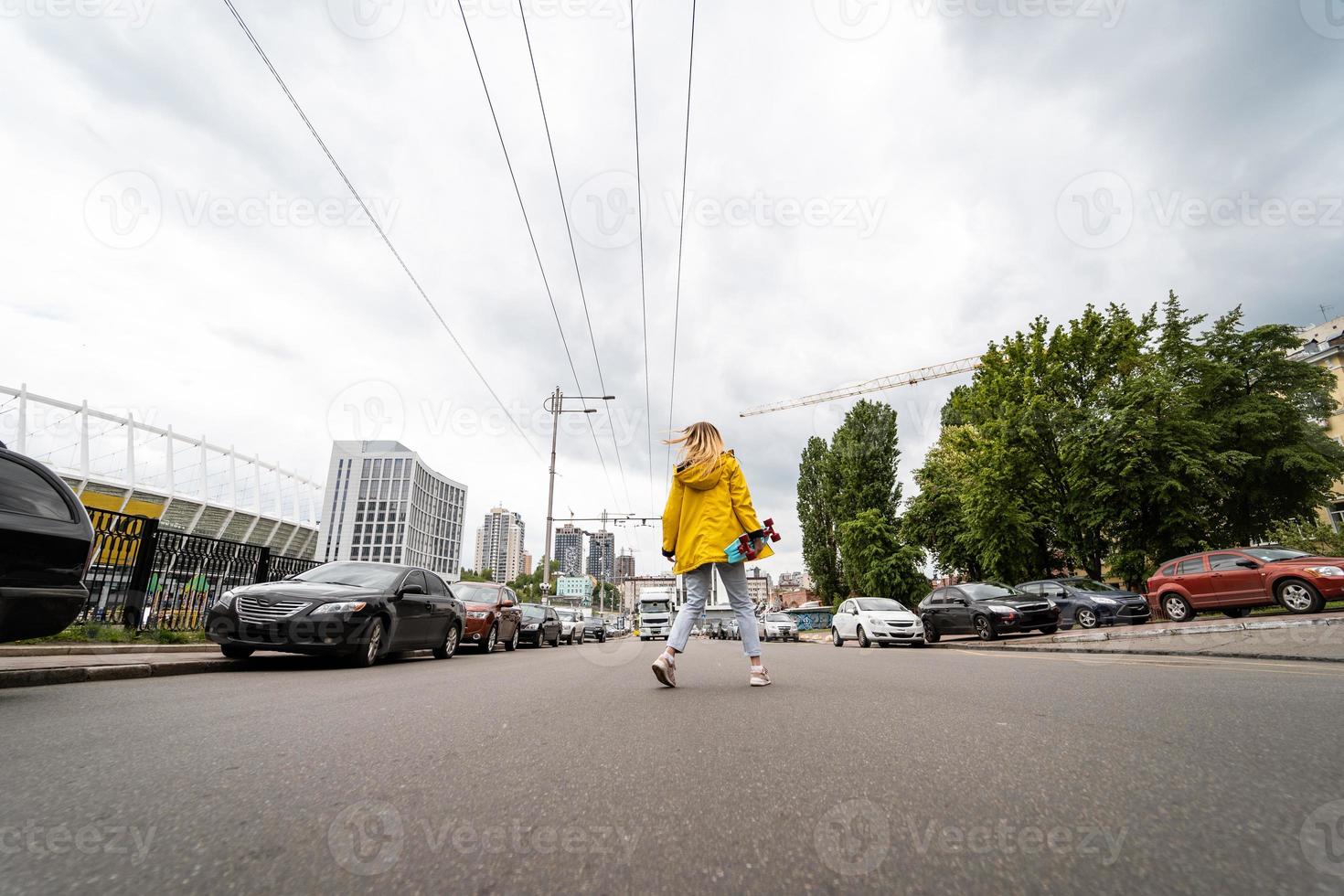 una hermosa joven sostiene una patineta y cruza la calle foto