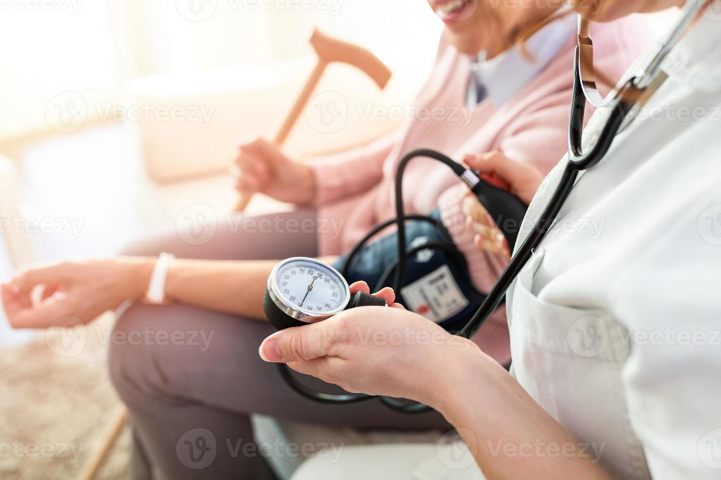 enfermera midiendo la presión arterial de la anciana en casa. sonriendo el uno al otro. joven enfermera midiendo la presión arterial de una anciana en casa. doctor revisando la presión arterial de una anciana foto