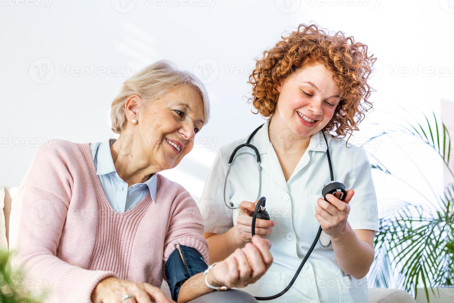 joven enfermera midiendo la presión arterial de una anciana en casa. enfermera controlando la presión arterial de una anciana en casa, cuidadora domiciliaria controlando la presión arterial de los pacientes foto