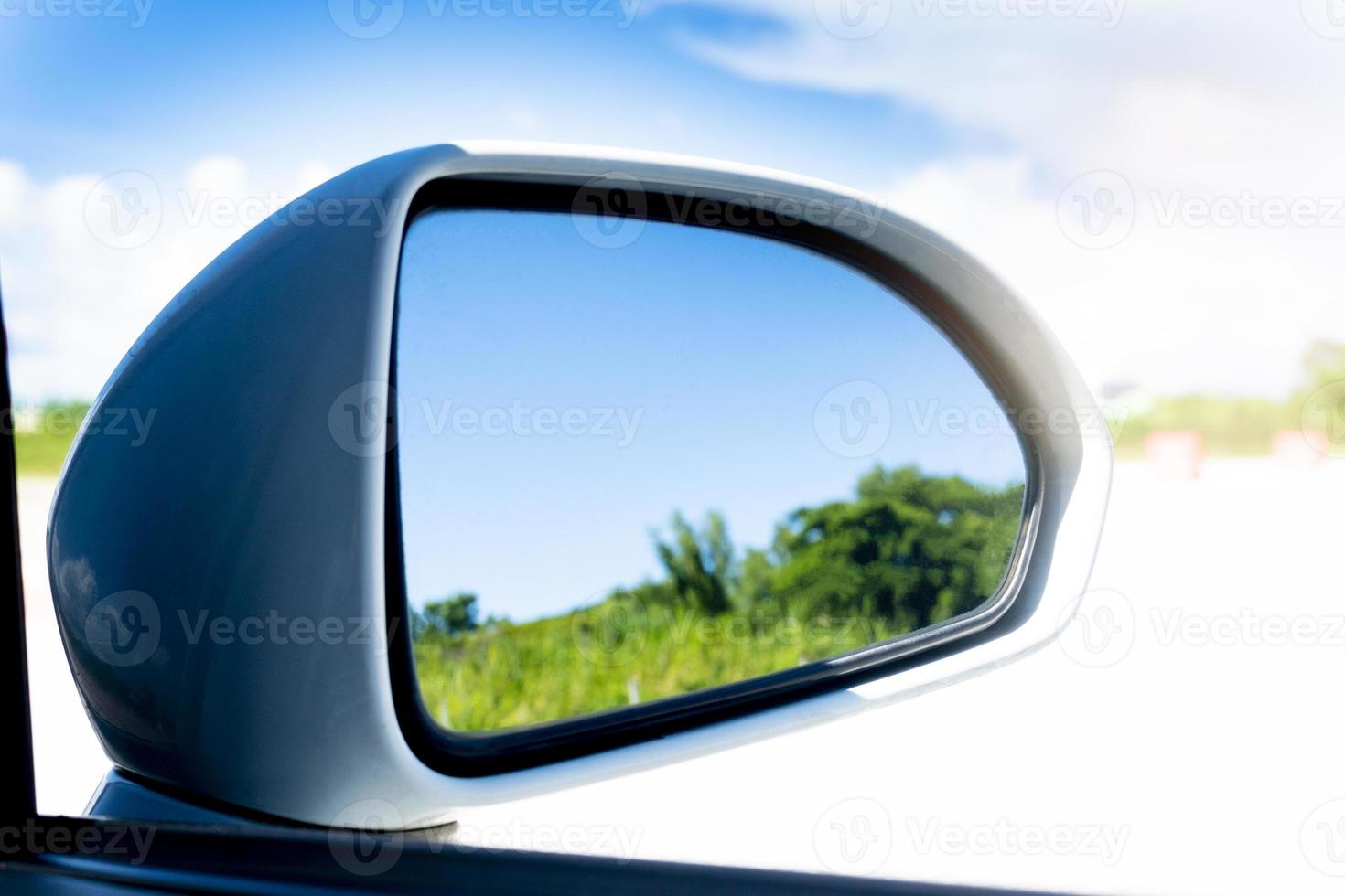 Mirror wing of white car with reflection of green trees blur in mirror. Under sky was bright and turquoise. Bright outdoor spaces. photo