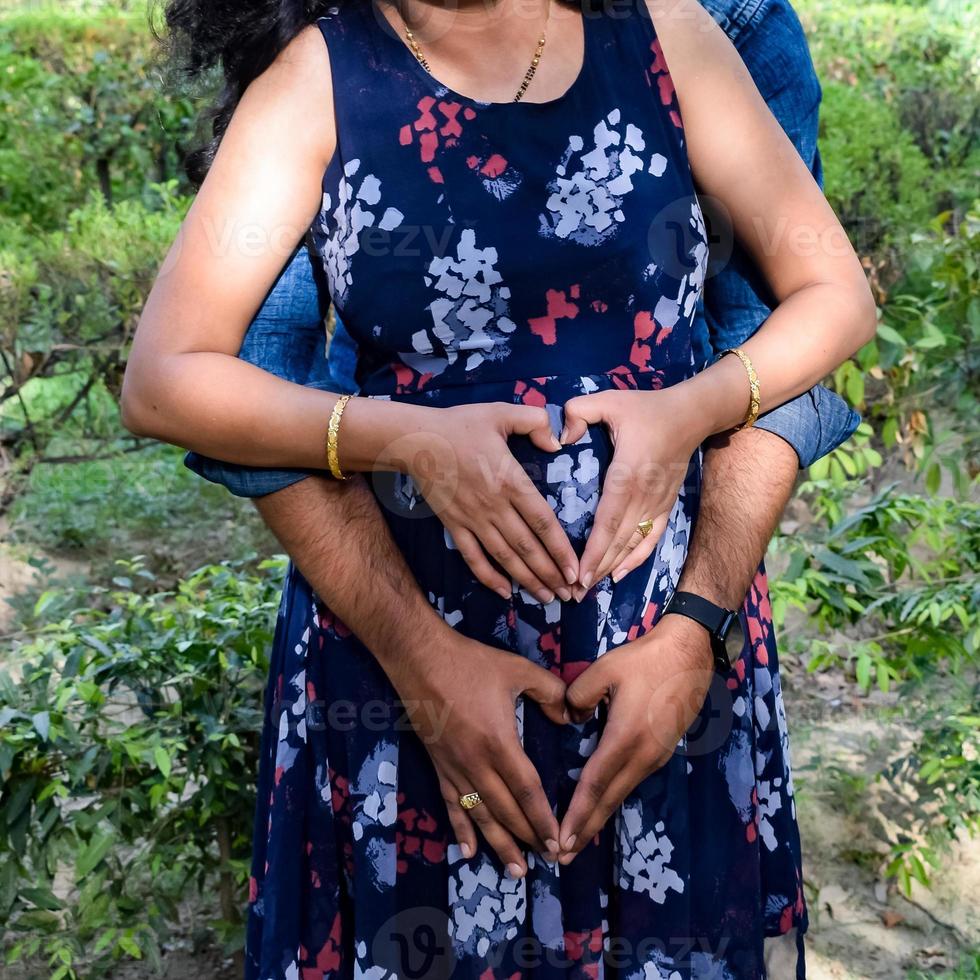 Indian couple posing for maternity baby shoot. The couple is posing in a lawn with green grass and the woman is falunting her baby bump in Lodhi Garden in New Delhi, India photo