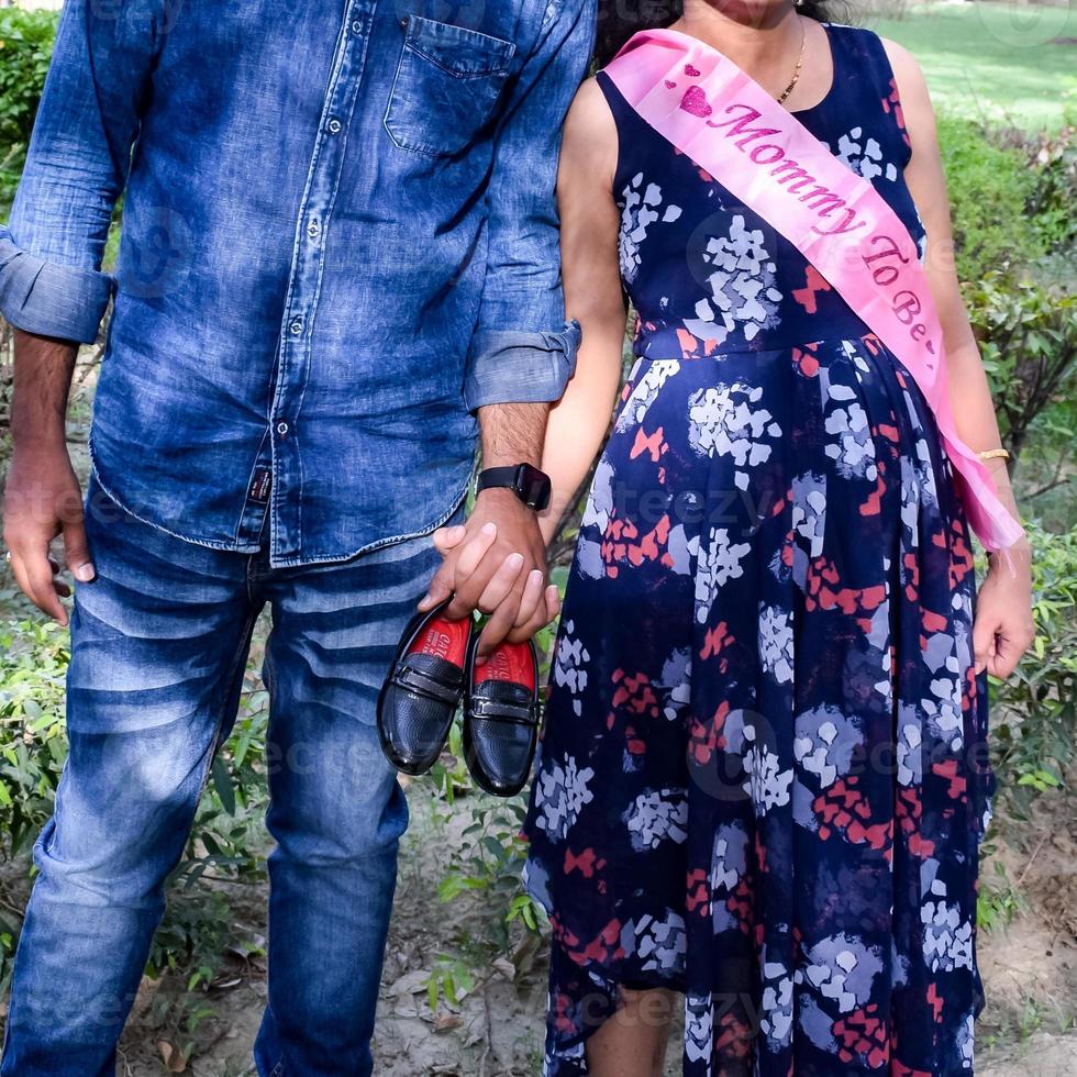 Indian couple posing for maternity baby shoot. The couple is posing in a lawn with green grass and the woman is falunting her baby bump in Lodhi Garden in New Delhi, India photo