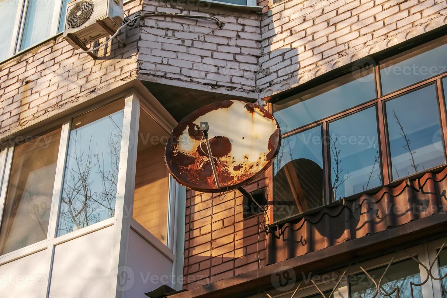 Old rusty satellite dish for television on a sunny day on the wall of the house. photo