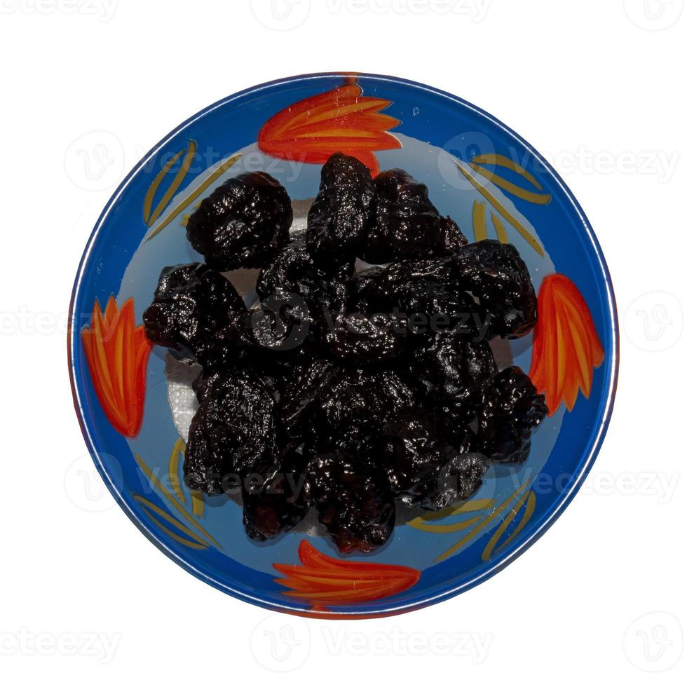 Dried black plums in glass bowl. Isolated on white background. Top view. photo