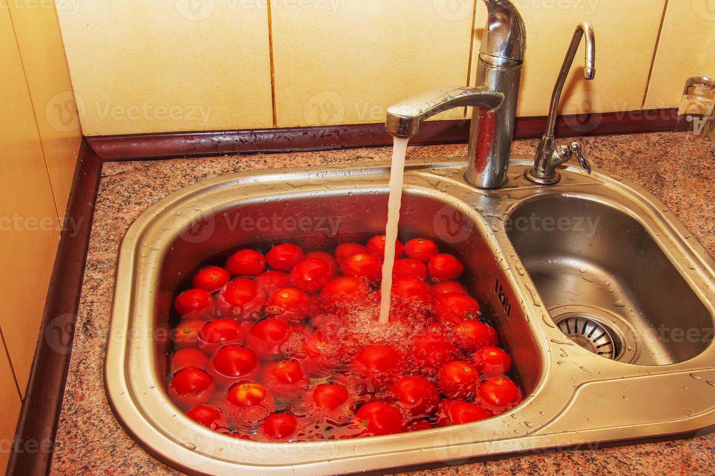 los tomates rojos frescos se lavan en agua en el fregadero de la cocina. foto