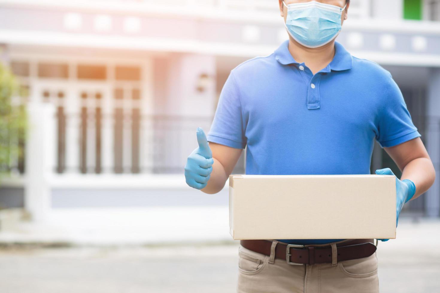 parcel delivery man wear protective gloves blue and mask, protect Hygiene germ and bacteria of a package through a service send to home. hand holding consign and submission customer accepting a of box photo