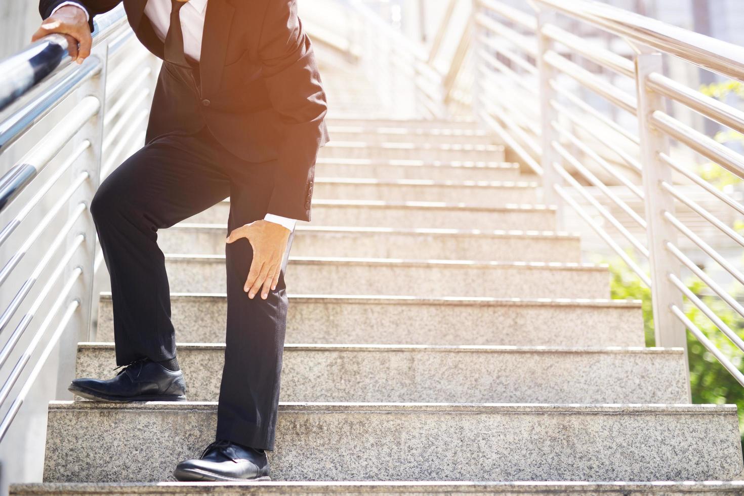 Businessman in a suit have the sore pain and painful knee problem expression and walk up and down on the stairway during go to office. Health care concept. photo