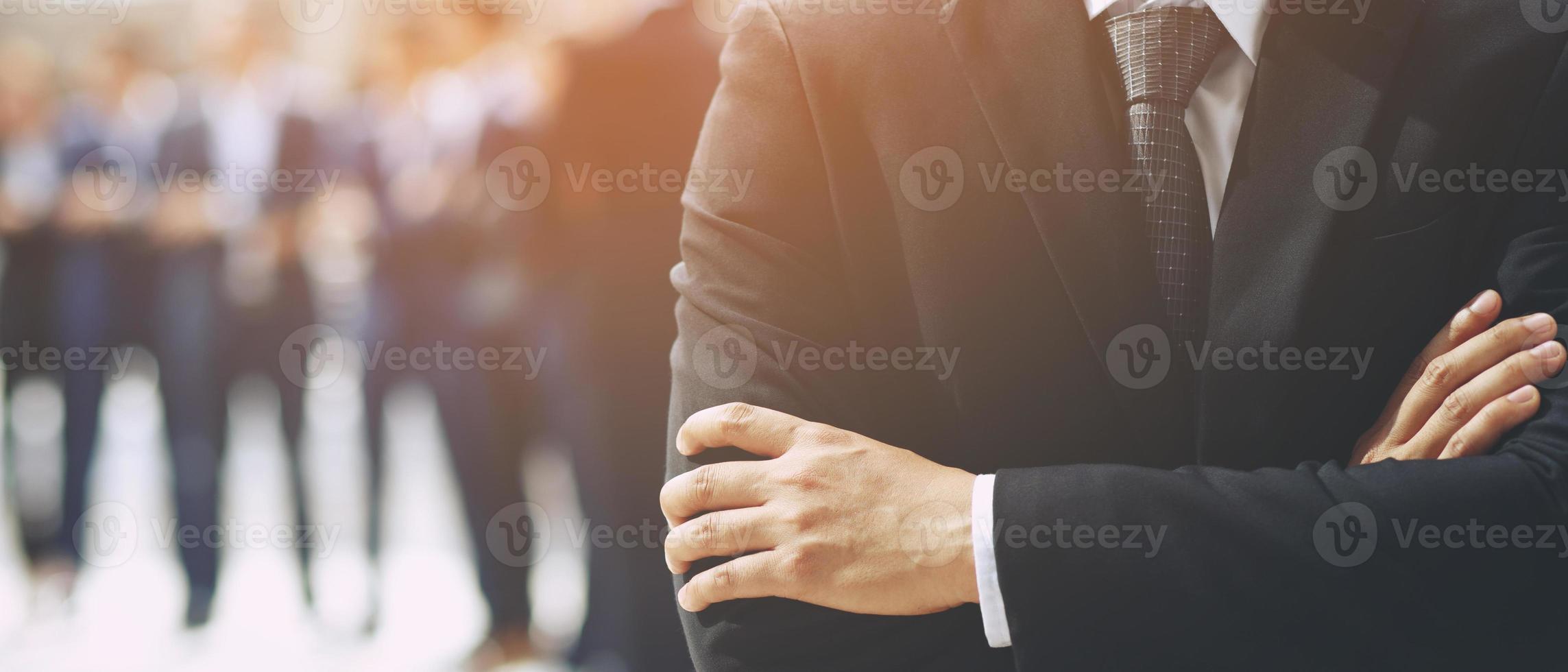 Portrait of a CEO businessman standing hand cross arm successful business team in a classic black suit with employee in background. photo