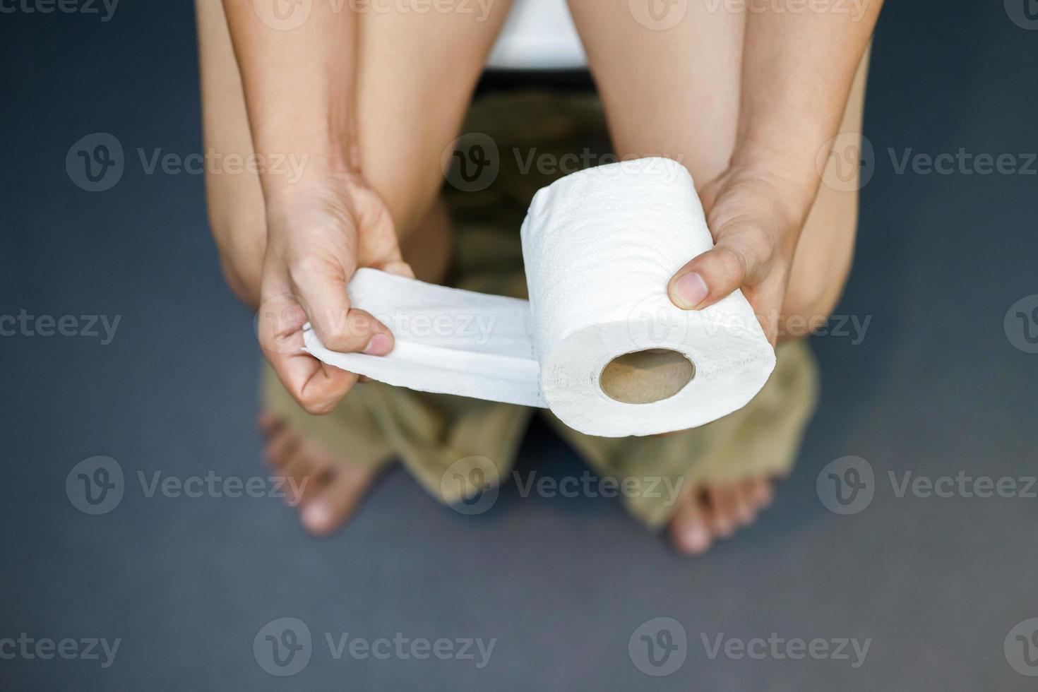 Man suffers from diarrhea hand hold tissue paper roll in front of toilet bowl. constipation in bathroom. Treatment stomach pain and Hygiene, health care photo